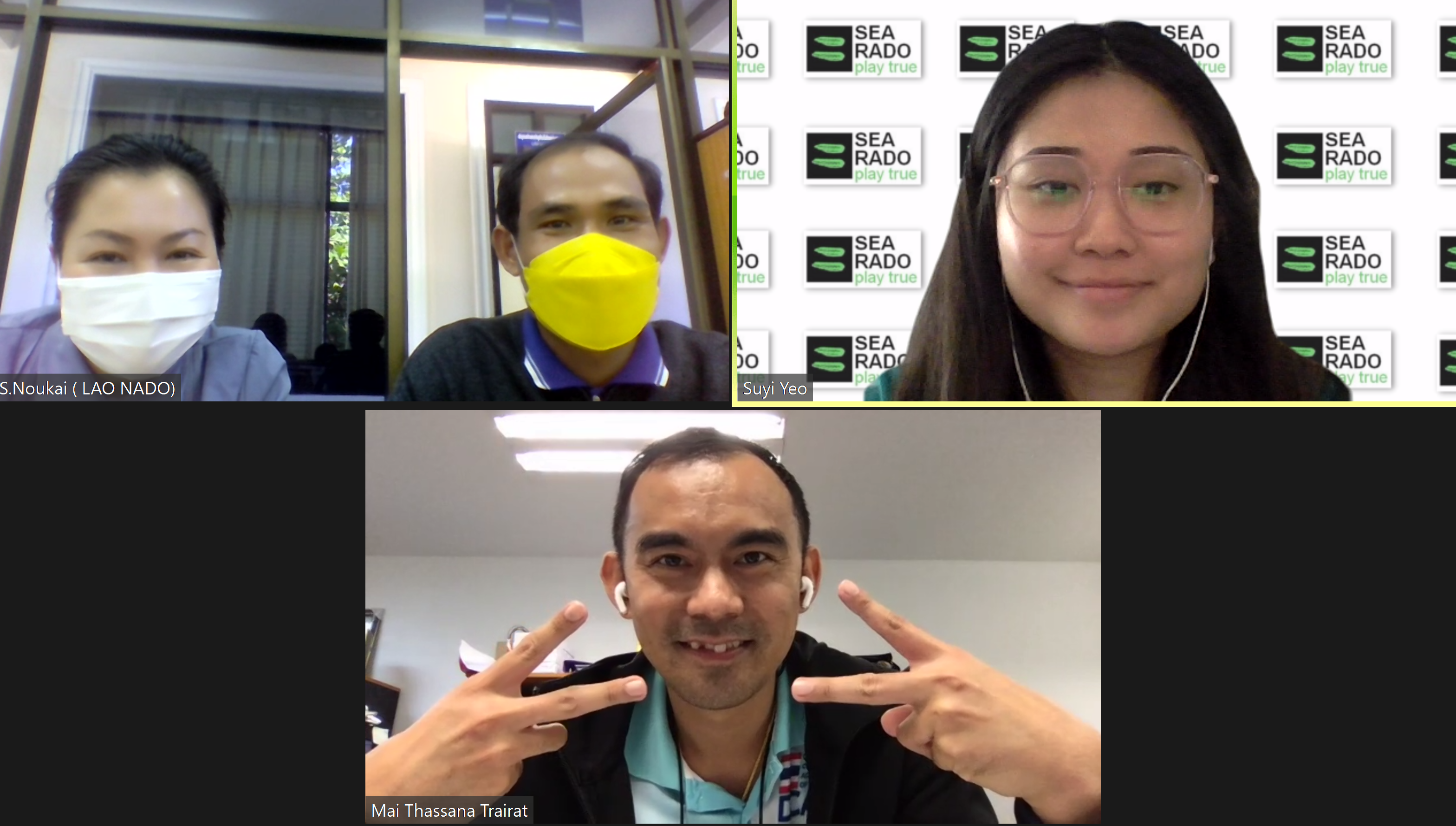 Four people on a video call, two wearing face masks, one woman with glasses before a SEA RADO banner, one man making peace signs.